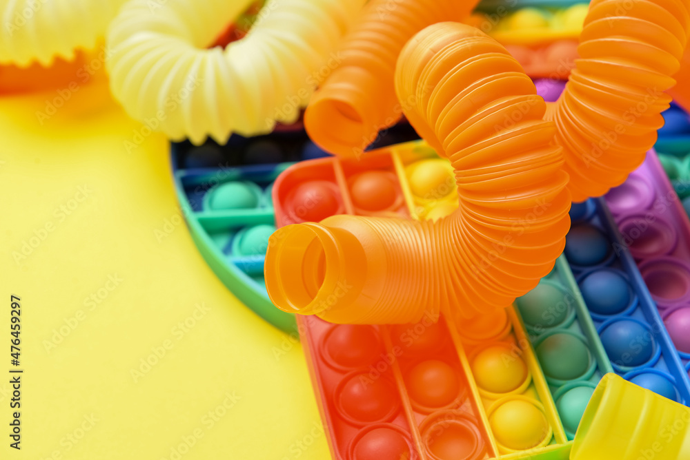 黄色背景下的彩色Pop Tubes和Pop-it坐立不安的玩具