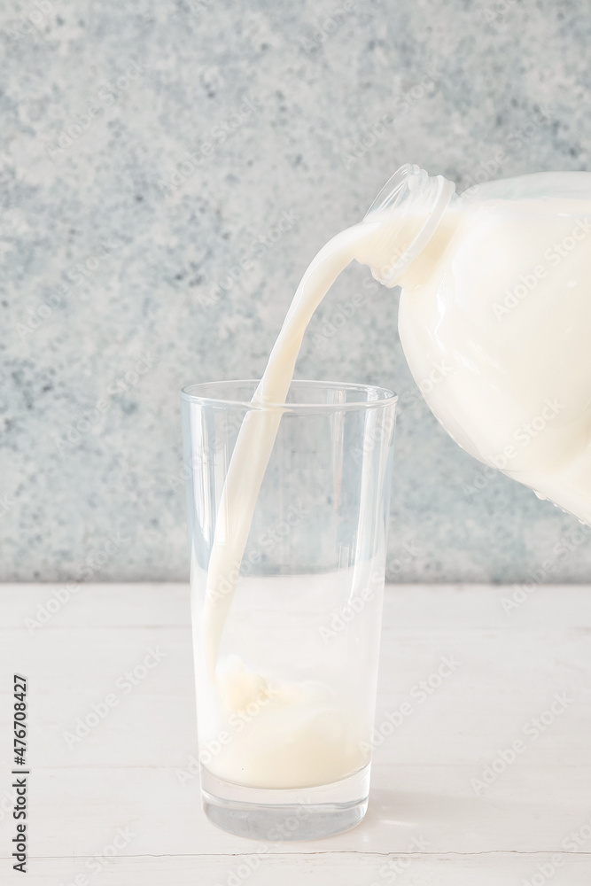 将牛奶从一加仑的容器倒入桌子上的玻璃杯