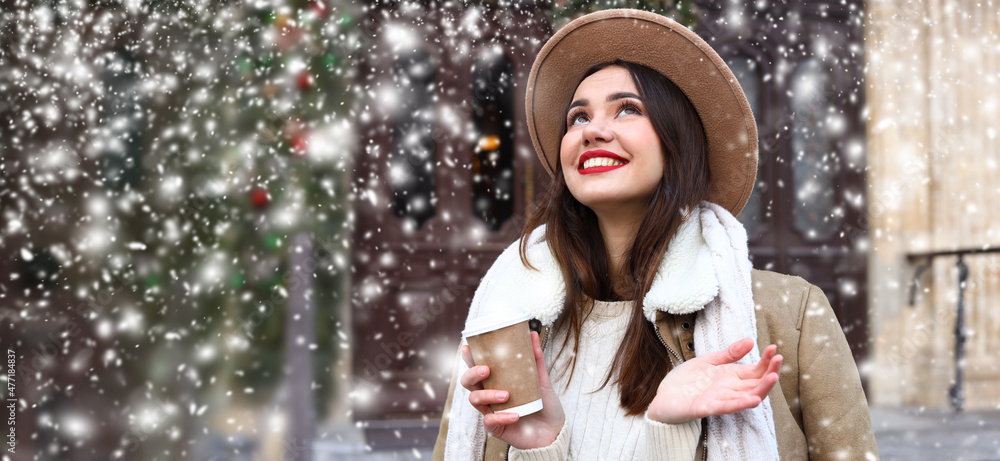 Happy young woman with cup of coffee on snowy day