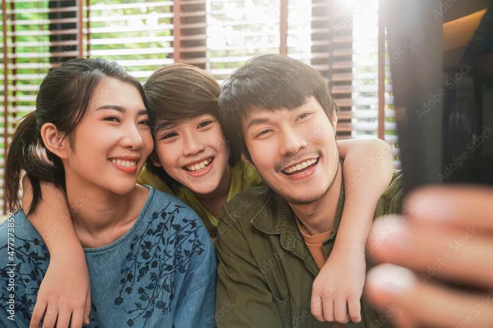 幸福的亚洲家庭在家里使用智能手机自拍或视频通话