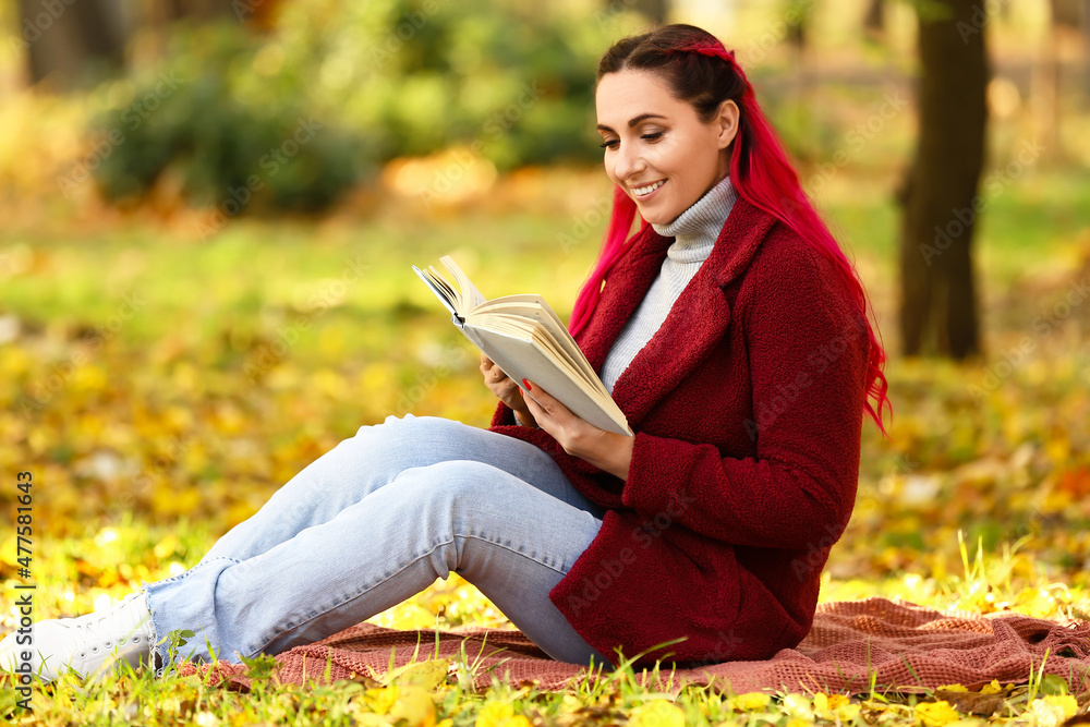 穿着保暖外套的美女在秋季公园看书