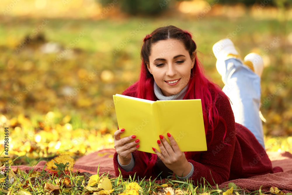 穿着温暖外套的美丽女人在秋天公园看书