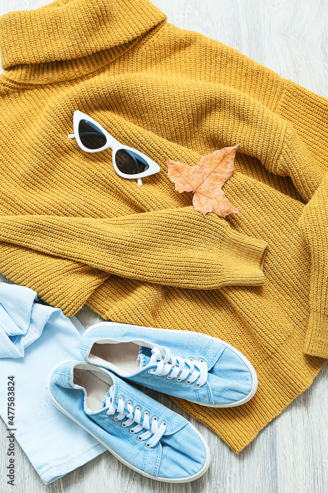 时尚的女性毛衣、牛仔裤、鞋子、太阳镜和浅木背景的秋叶，特写