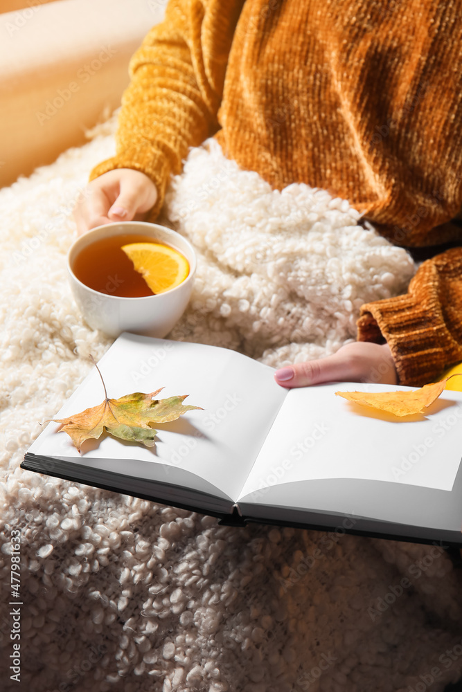 披着格子布的女人拿着一杯茶和一本秋叶书，特写