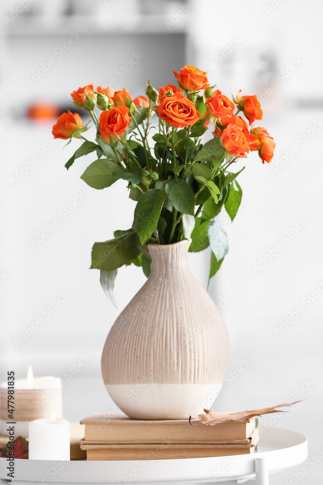 房间桌子上放着漂亮的橙色玫瑰、书籍和蜡烛的花瓶