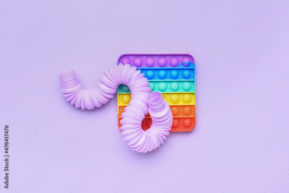 紫色背景下的彩色Pop Tube和Pop-it坐立不安的玩具