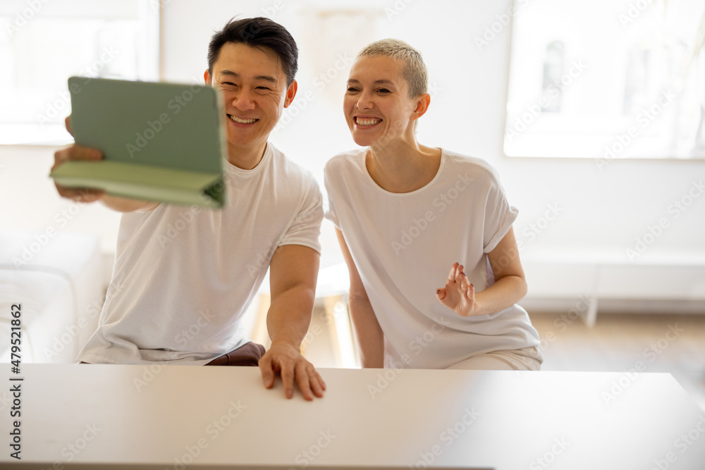 微笑的多种族夫妇在家里用数字平板电脑进行视频通话。家庭生活的概念
