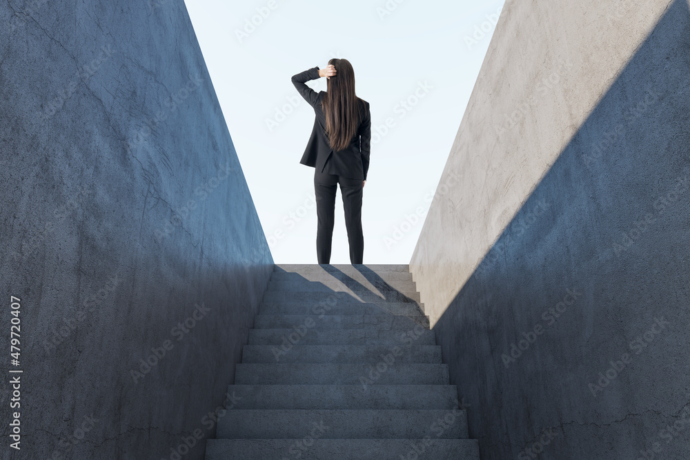 体贴的女人站在抽象的混凝土楼梯上，在阳光下走向成功的背影。