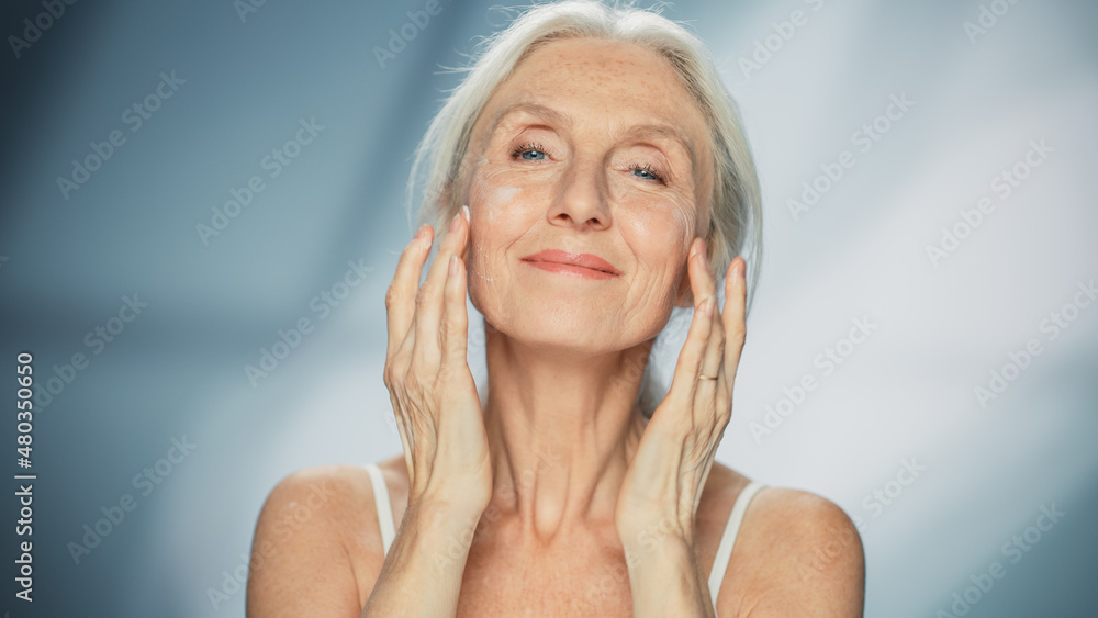 Portrait of Beautiful Senior Woman Gently Applying Face Cream. Elderly Lady Makes Her Skin Soft, Smo