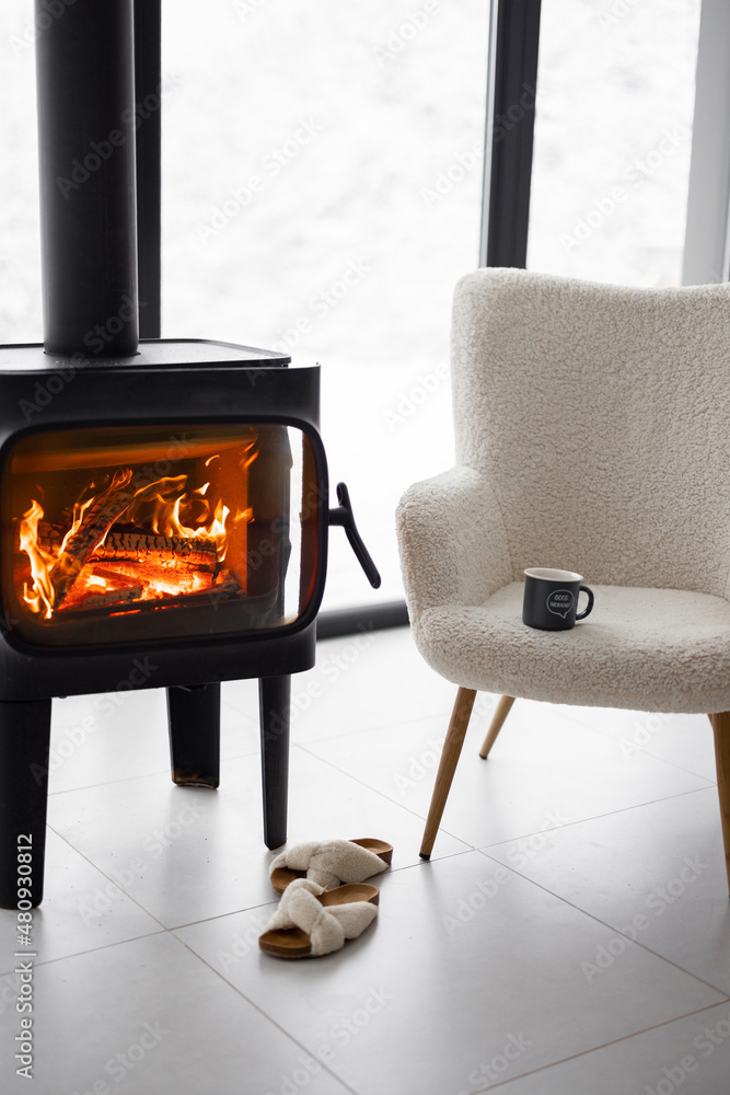 燃烧的壁炉旁舒适的生活空间，以雪地为背景，配有椅子、杯子和拖鞋