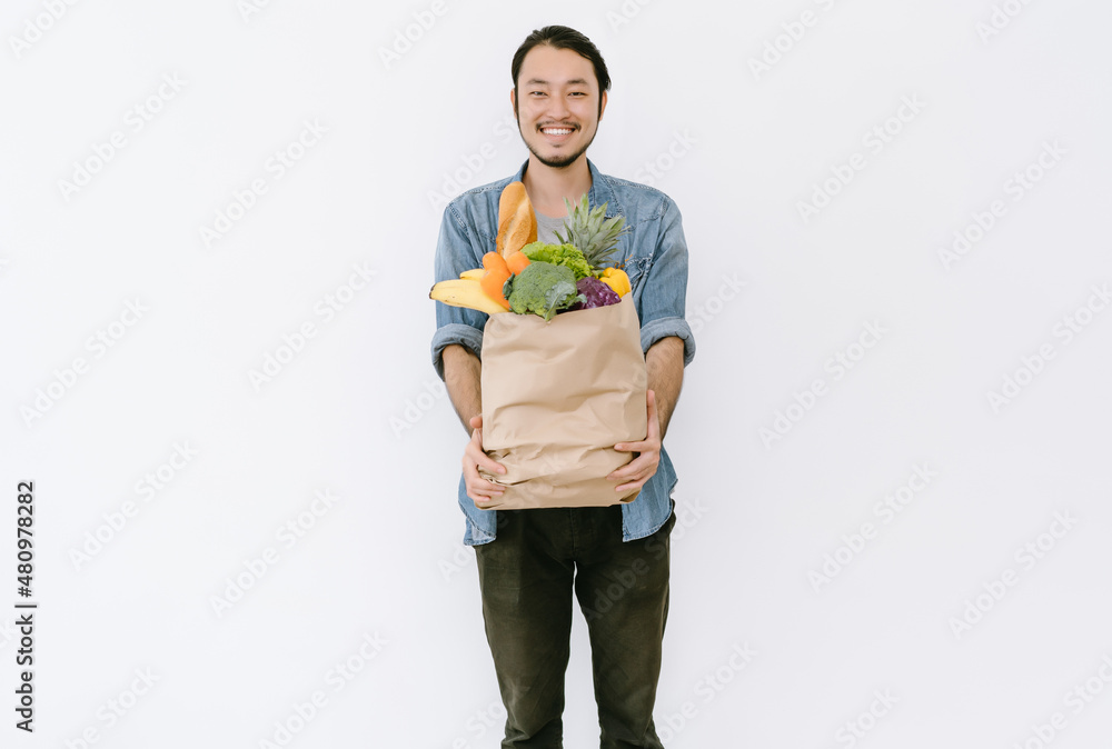 健康积极的亚洲年轻男子拿着装满新鲜蔬菜和杂货的购物袋