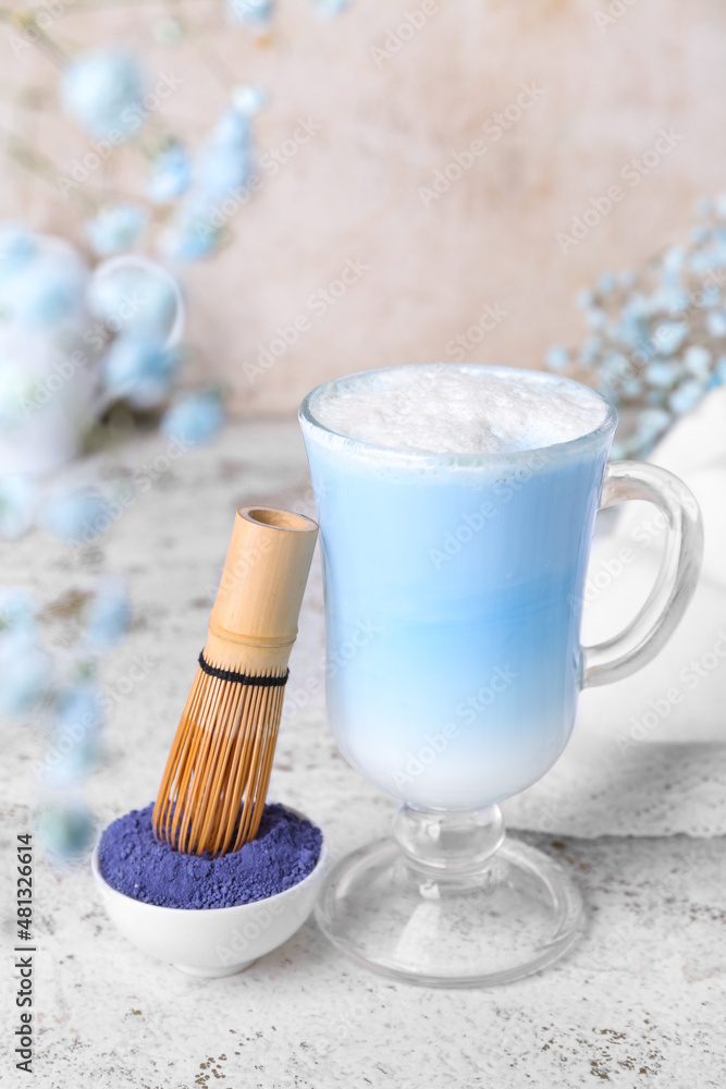 Glass of blue matcha latte, powder and chasen on light background