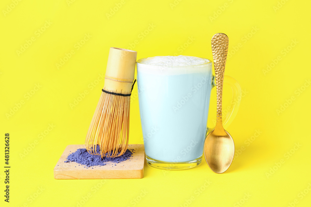 一杯蓝色抹茶拿铁，粉末，奶油和勺子，黄色背景