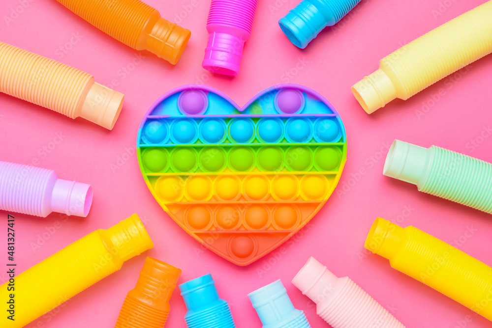 粉色背景下的彩色Pop Tubes和Pop-it坐立不安的玩具