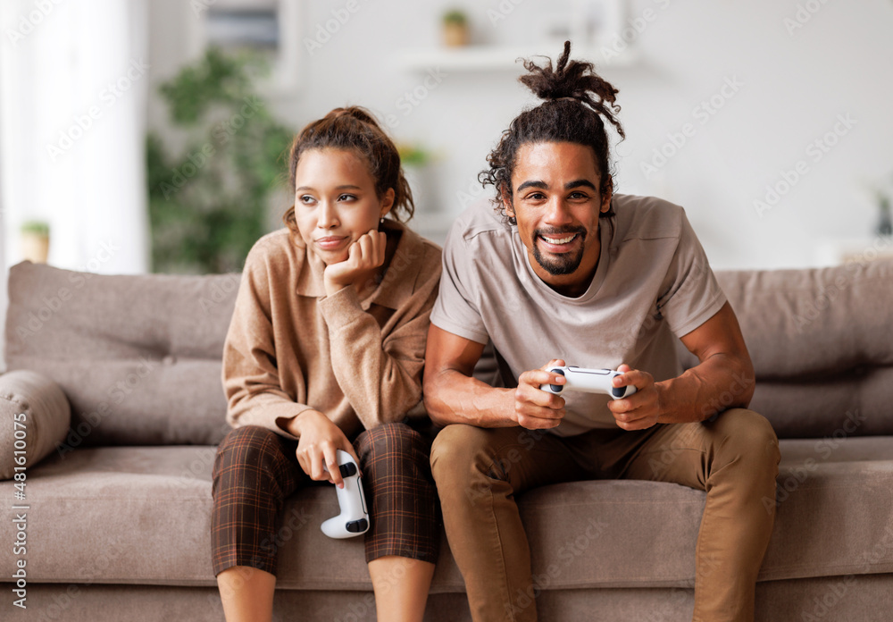 无聊的约会。兴奋的非裔美国男子在玩电子游戏，却忽视了坐在旁边无聊的女人