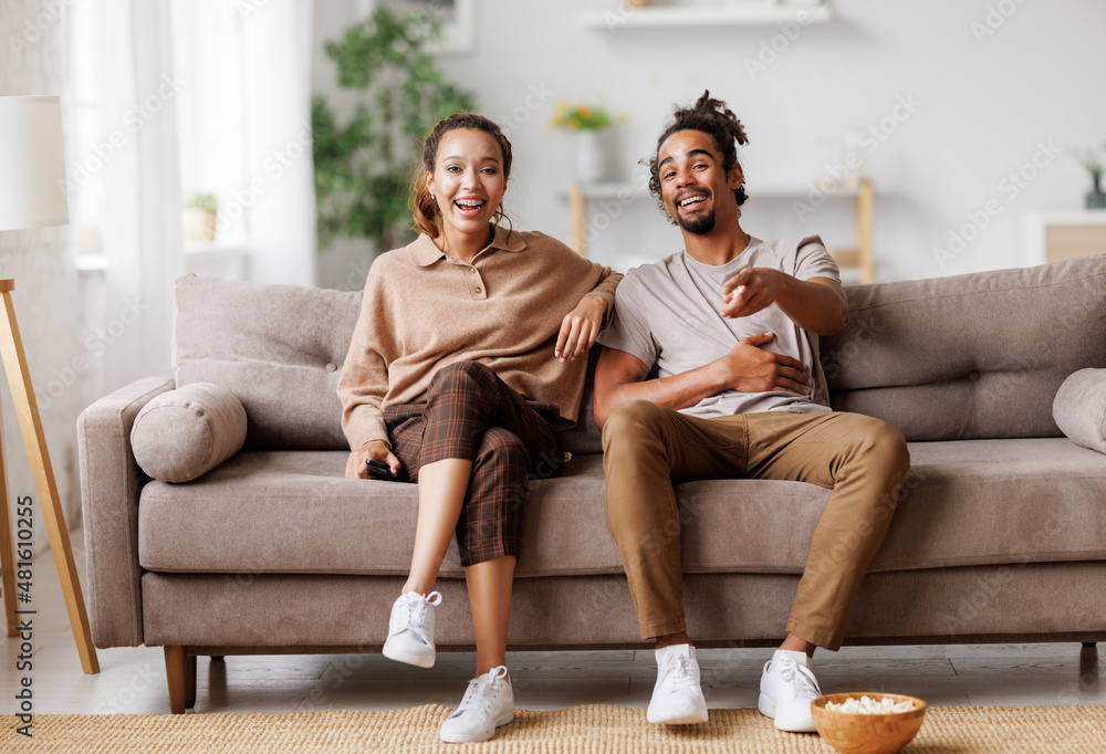 Young overjoyed african american couple at home watching comedy movie, laughing out of loud