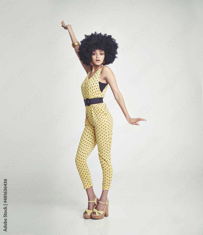 Feeling the 70s vibe. A young woman wearing a 70s retro jumpsuit and striking a disco pose while in 
