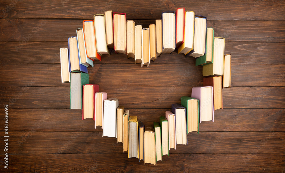 Love of books reading. Stack of books in the colored cover lay on the table in the shape of a heart.