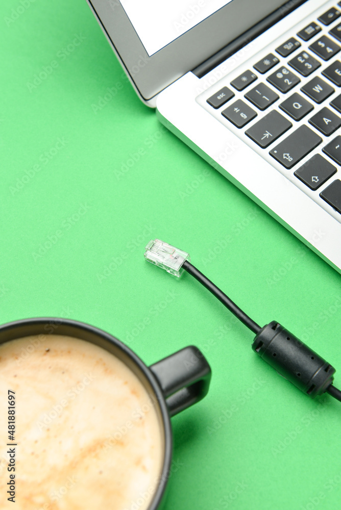 Cup of coffee, internet cable and laptop on green background