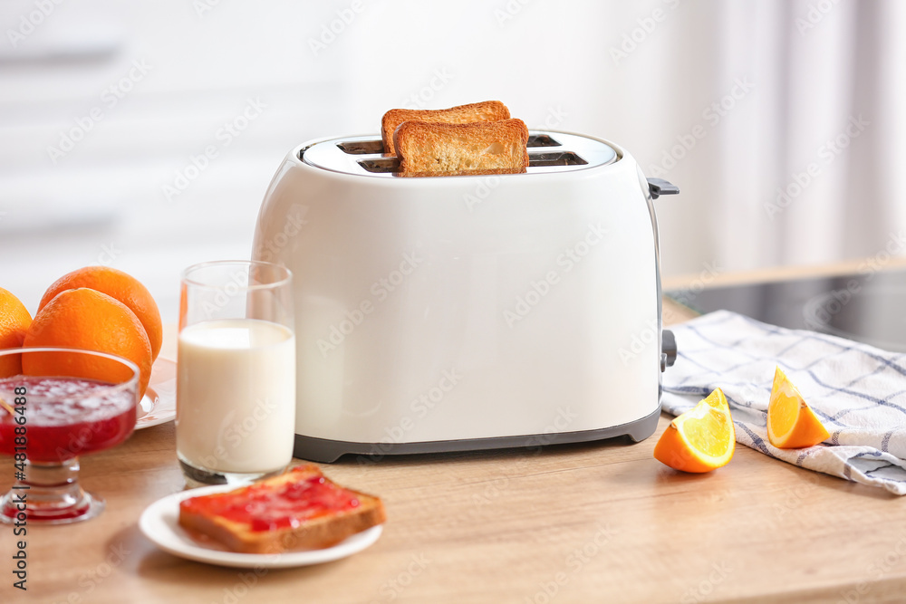 White toaster with tasty breakfast on table in light kitchen