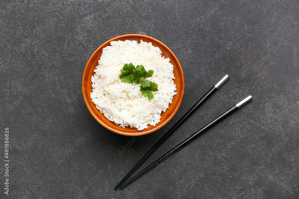 Bowl with tasty boiled rice and chopsticks on dark background