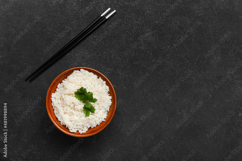 深色背景下有美味的煮米饭和筷子的碗