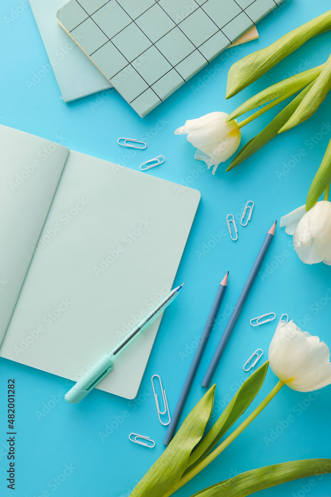 用空白笔记本、文具和彩色背景上美丽的郁金香组成
