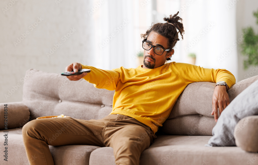 疲惫的非洲裔美国男子在家放松时用遥控器切换电视频道