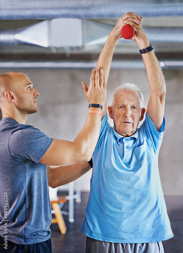 长寿举重。一名老年男子在教练的帮助下锻炼的照片。
