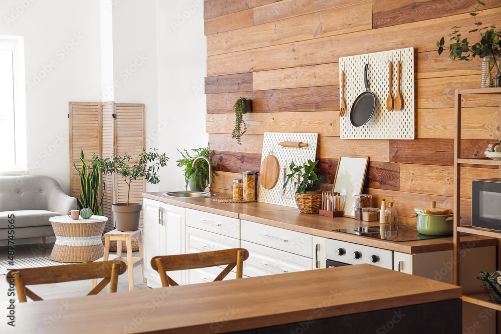 Interior of modern kitchen with white counters, peg boards and wooden wall