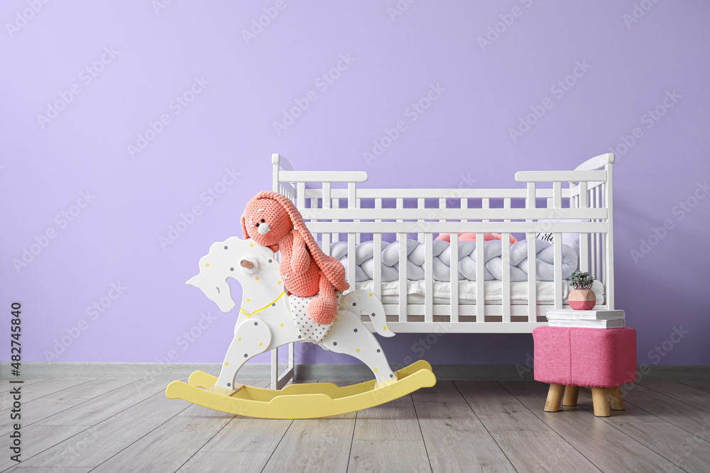 可爱的玩具兔子坐在木马上，在彩色墙上放着书和婴儿床
