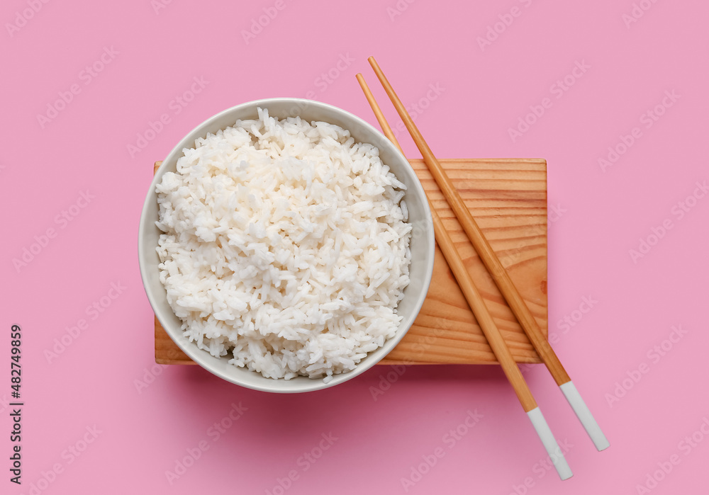 碗里有美味的煮米饭和粉红色背景的筷子