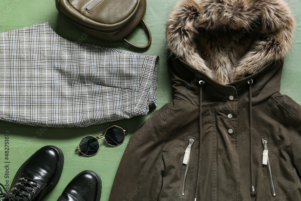 绿色木质背景的冬季夹克、裤子、背包、鞋子和太阳镜