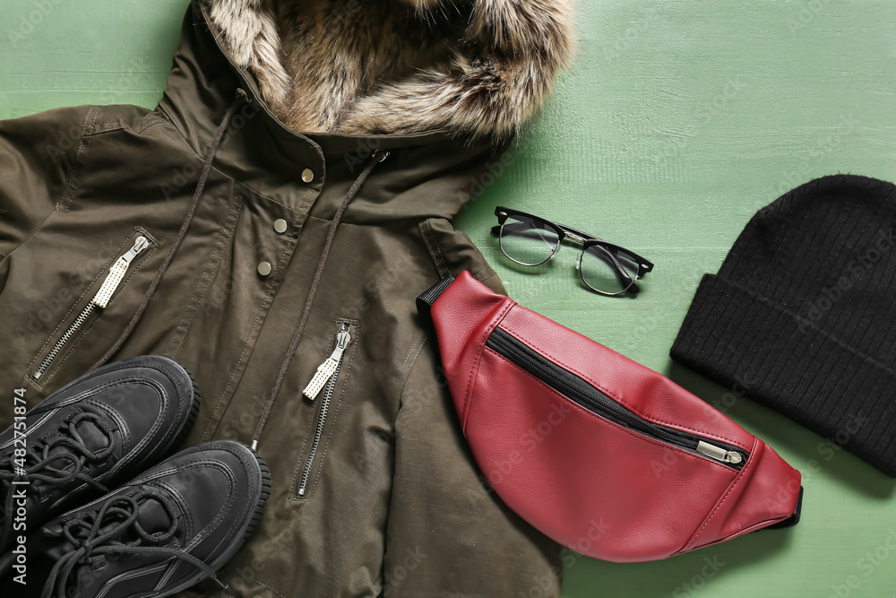 绿色木质背景的冬季夹克、眼镜、帽子、包包和鞋子