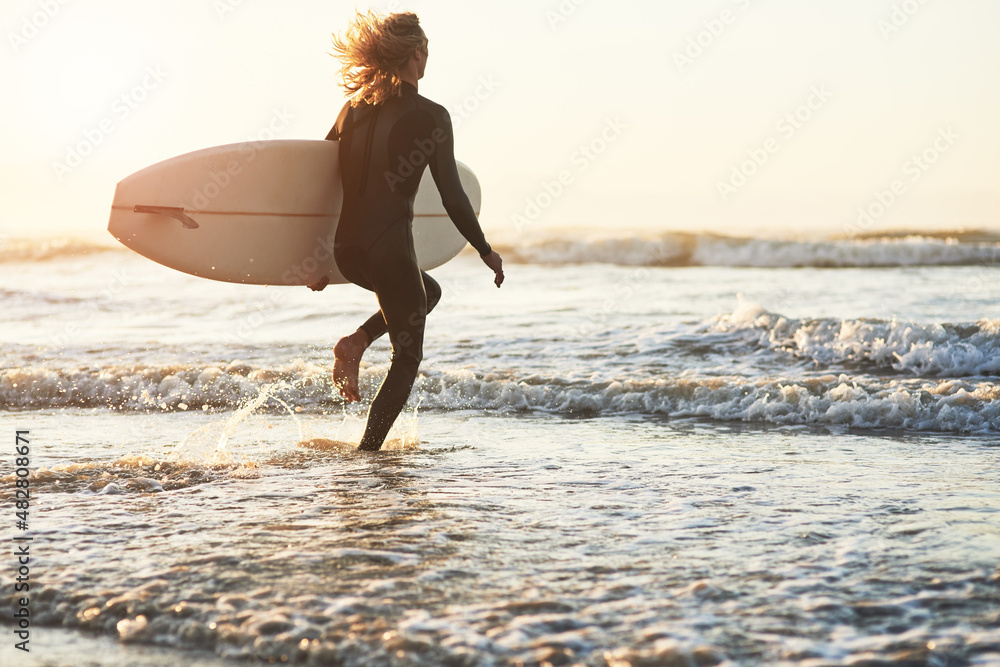 脱离世界。一个年轻人在海滩冲浪的后视镜头。