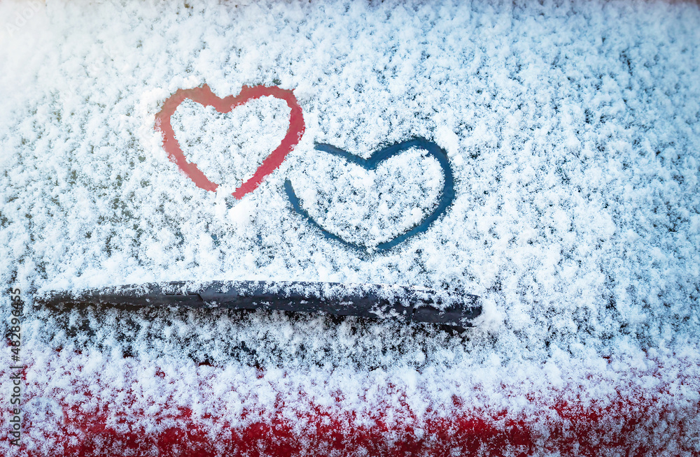 两颗心（爱的象征）画在汽车挡风玻璃雨刷上方的雪地上。情人节