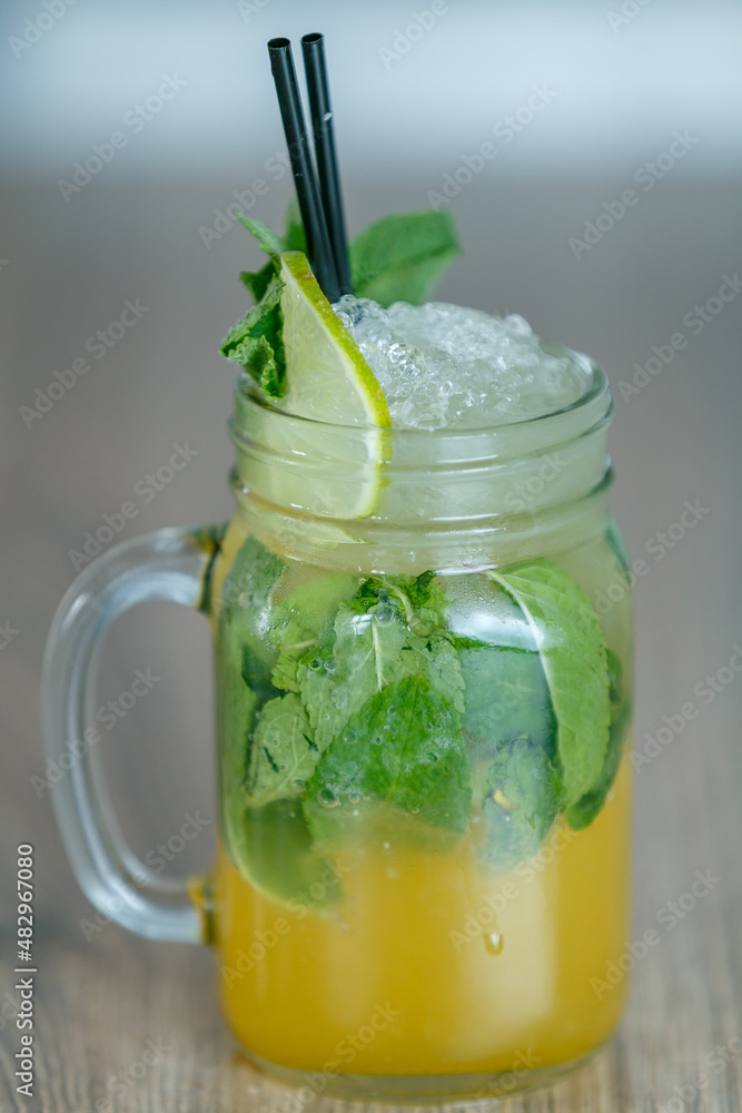 Fresh lemon and mint lemonade with crushed ice and lime and straw on table with blueish background