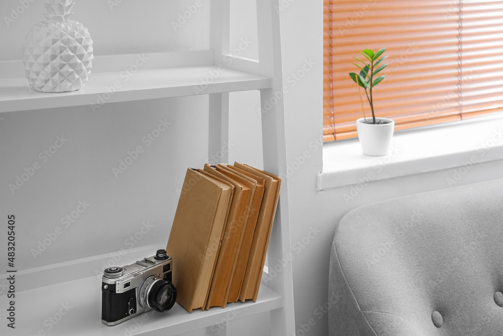 Photo camera and books on shelf near light wall