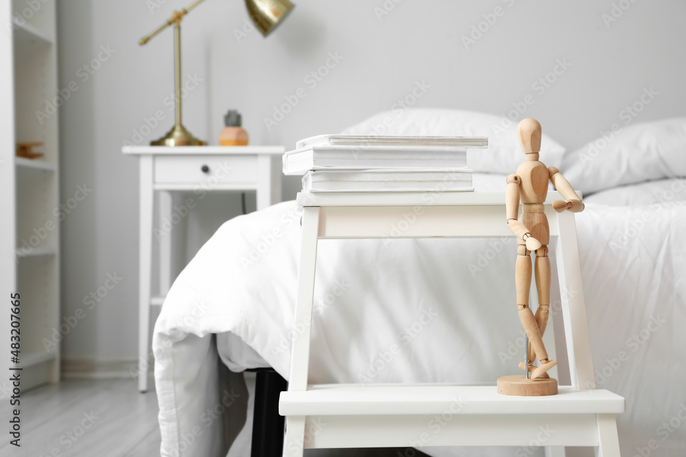 房间里靠近床的带书和木制人体模型玩偶的阶梯凳