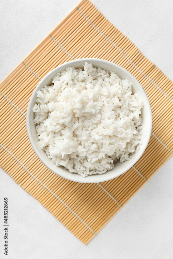 Bowl with tasty boiled rice and mat on light background