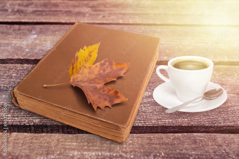 a cup of tea and a book on a wooden surface against the background of fallen leaves, autumn season