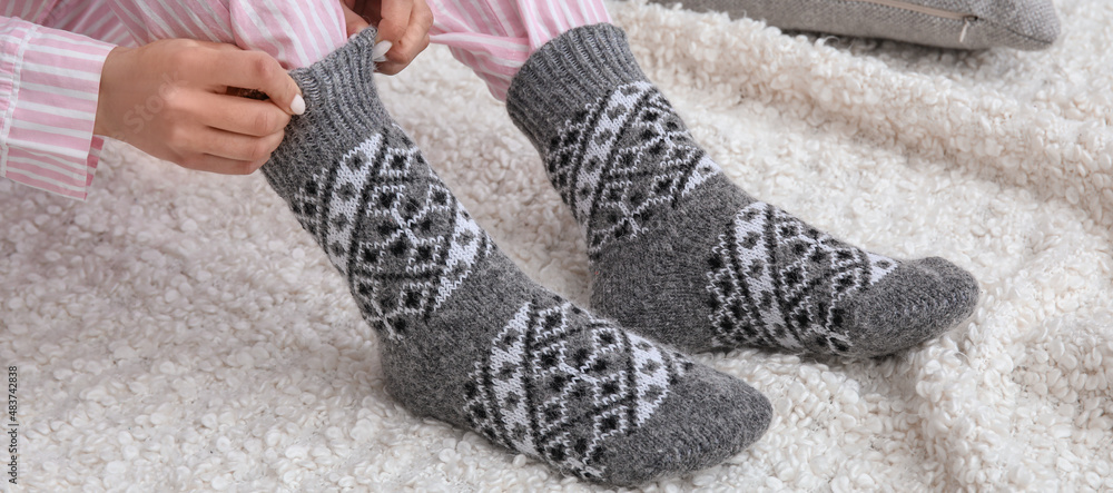 Woman putting on her warm knitted socks at home. Concept of heating season