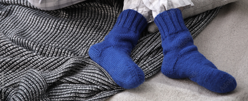 穿着保暖针织袜子的女人坐在家里的格子布上。供暖季节的概念