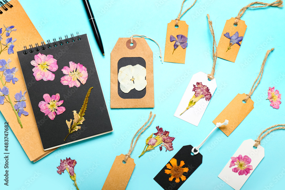 Dried pressed flowers with tags and notebooks on turquoise background