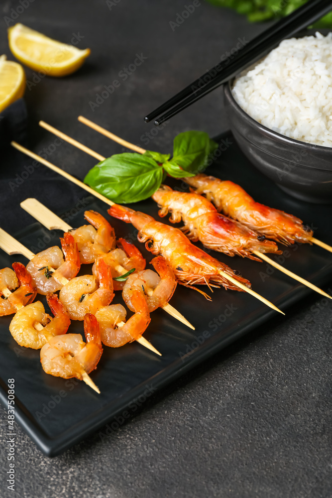 Board with tasty grilled shrimp skewers and rice on black background
