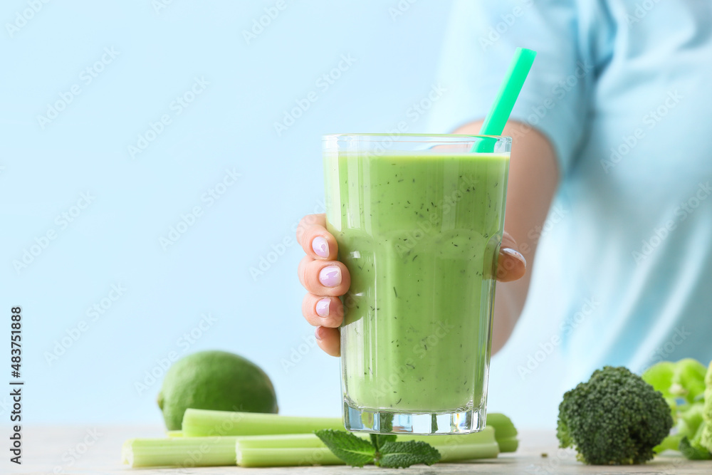一位女士在餐桌旁拿着一杯健康的绿色果汁，特写镜头