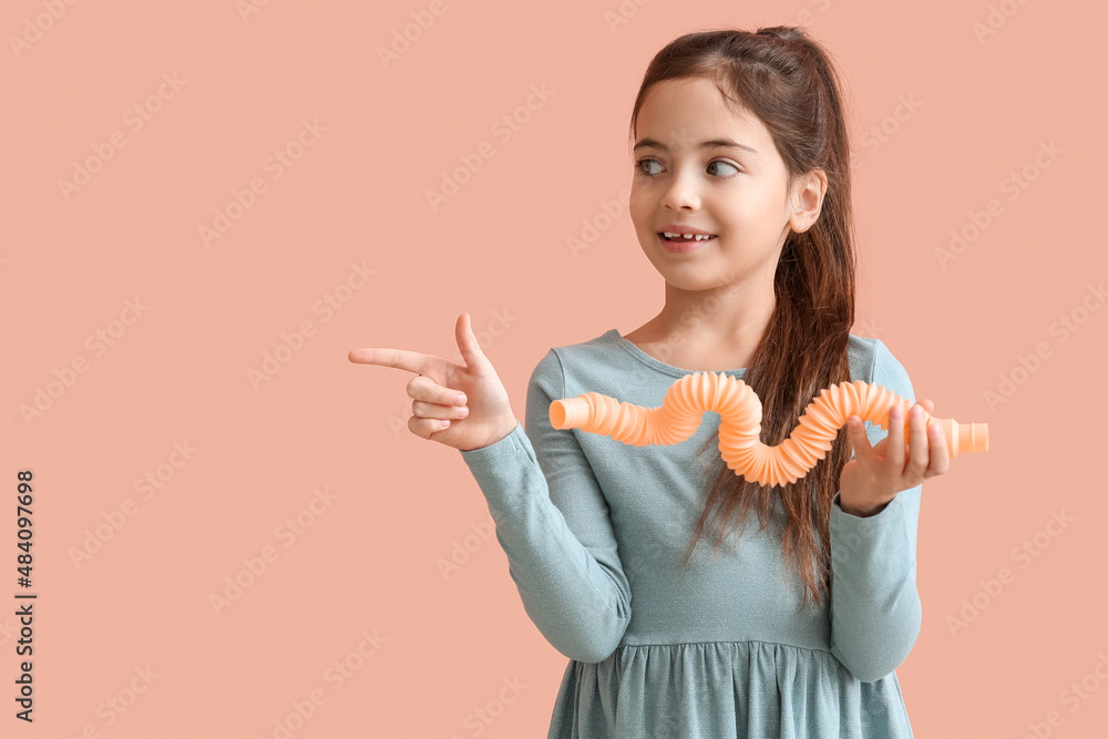 Funny little girl with Pop Tube pointing at something on pink background
