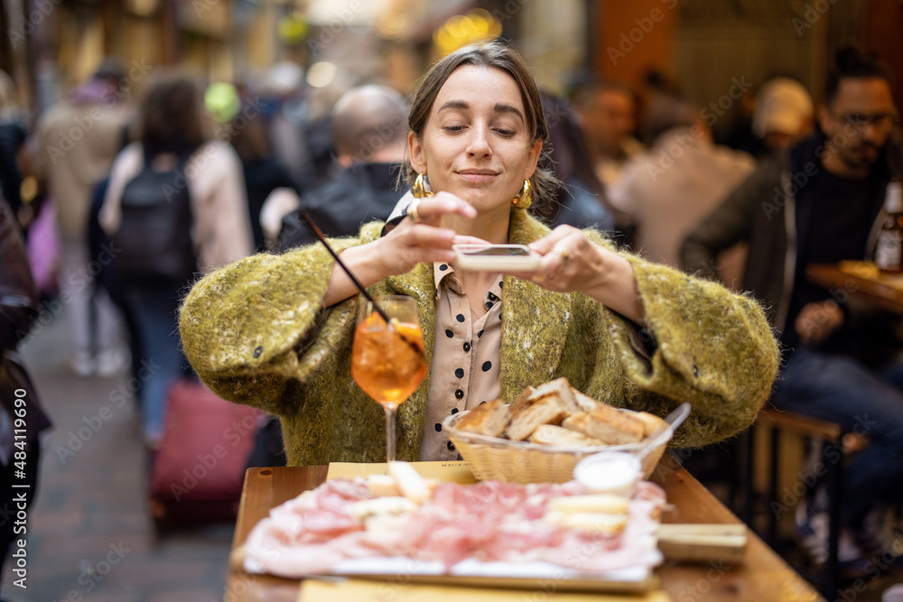 坐在餐厅里，一位女士拿着意大利肉类开胃菜和雪碧Aperol饮料拍照