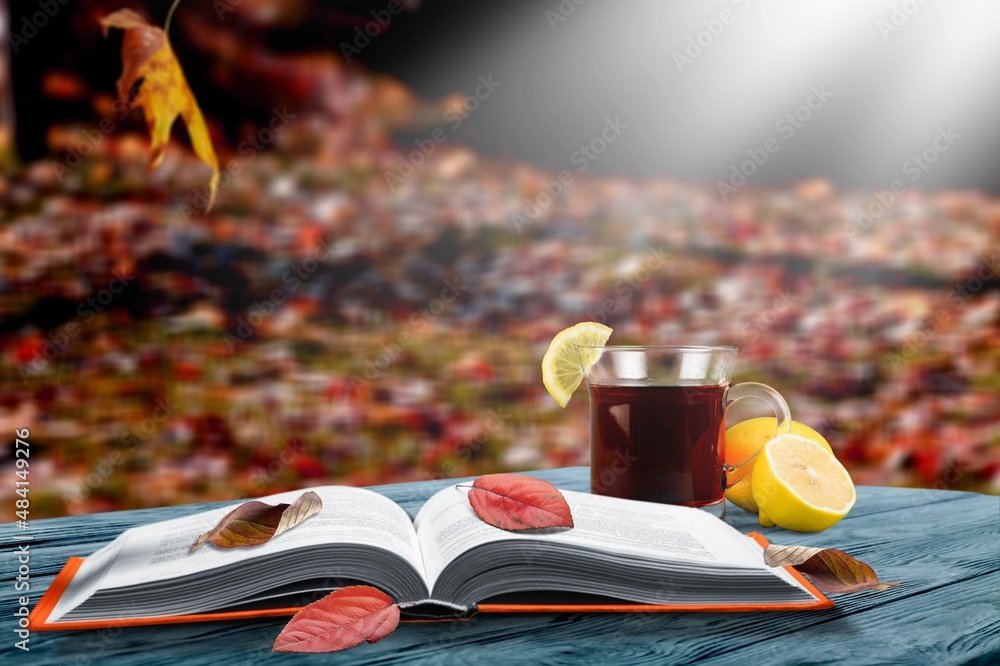 一杯茶和一本书，在落叶的背景下，在木制表面上，秋天的季节