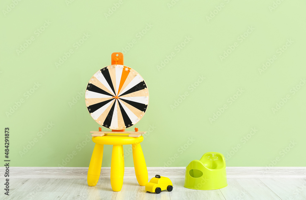 在靠近彩色墙的灰色木地板上，有命运之轮的便盆、玩具车和桌子